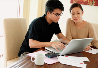 Young couple at the kitchen table using the online savings tool on their laptop.
