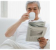 Un homme d'âge moyen dans son salon, lisant le journal et buvant une tasse de café.