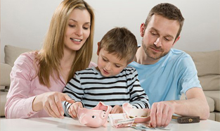 Un jeune couple assis à la table de cuisine avec son fils, ouvrant une tirelire à l'aide d'un marteau.