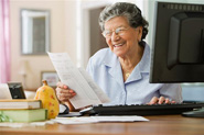 Personne âgée effectuant ses opérations bancaires sur son ordinateur de bureau à la maison.