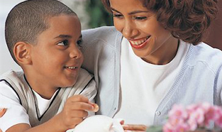 A little boy learns how to save by putting a coin into his piggy bank while mom smiles encouragingly.