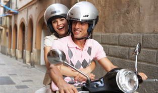 Young couple wearing helmets while riding their moped through a quiet street.